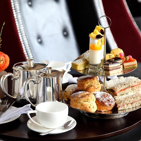 맥도날드 배스 스파 호텔 바스 외부 사진 The photo depicts an elegantly arranged afternoon tea setting. There is a tiered stand filled with a variety of treats, including scones, sandwiches, and small desserts like cakes and pastries. Accompanying this is a teapot and a cup on the table, su