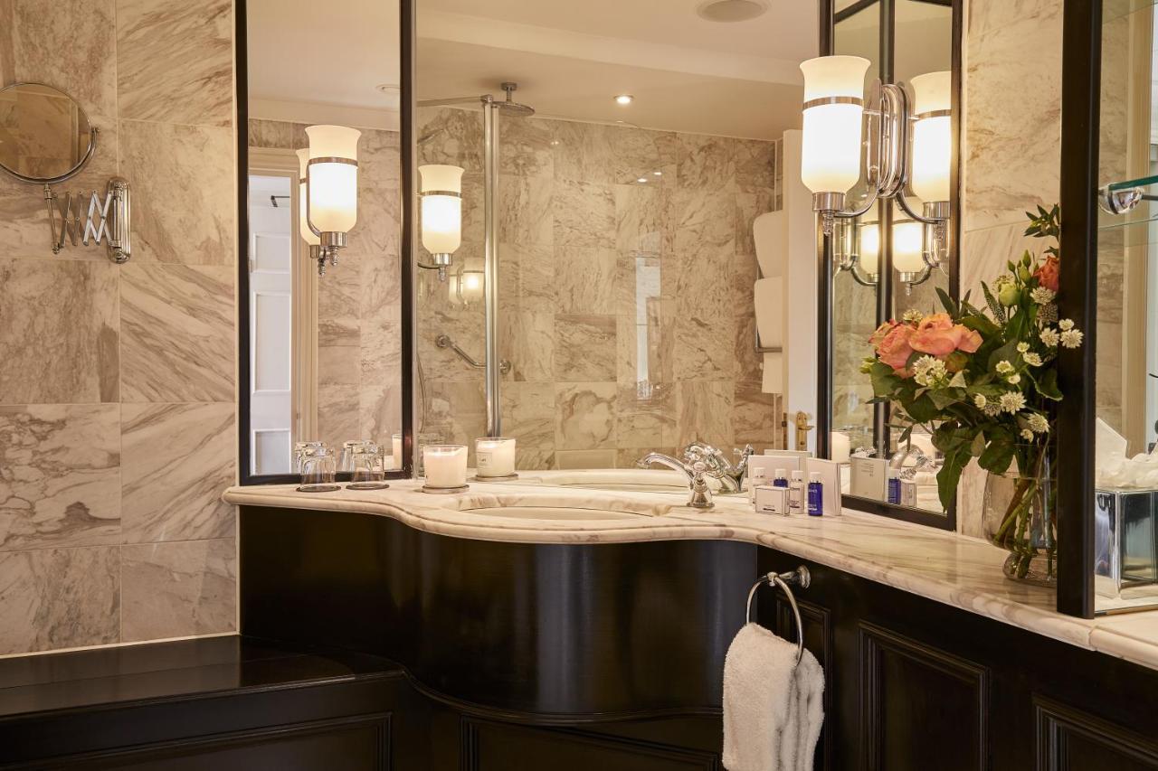맥도날드 배스 스파 호텔 바스 외부 사진 The photo shows a luxurious bathroom featuring elegant design elements. There is a curved marble countertop with a sink, complemented by stylish silver fixtures. The walls are adorned with light-colored marble, creating a sophisticated ambiance. Seve