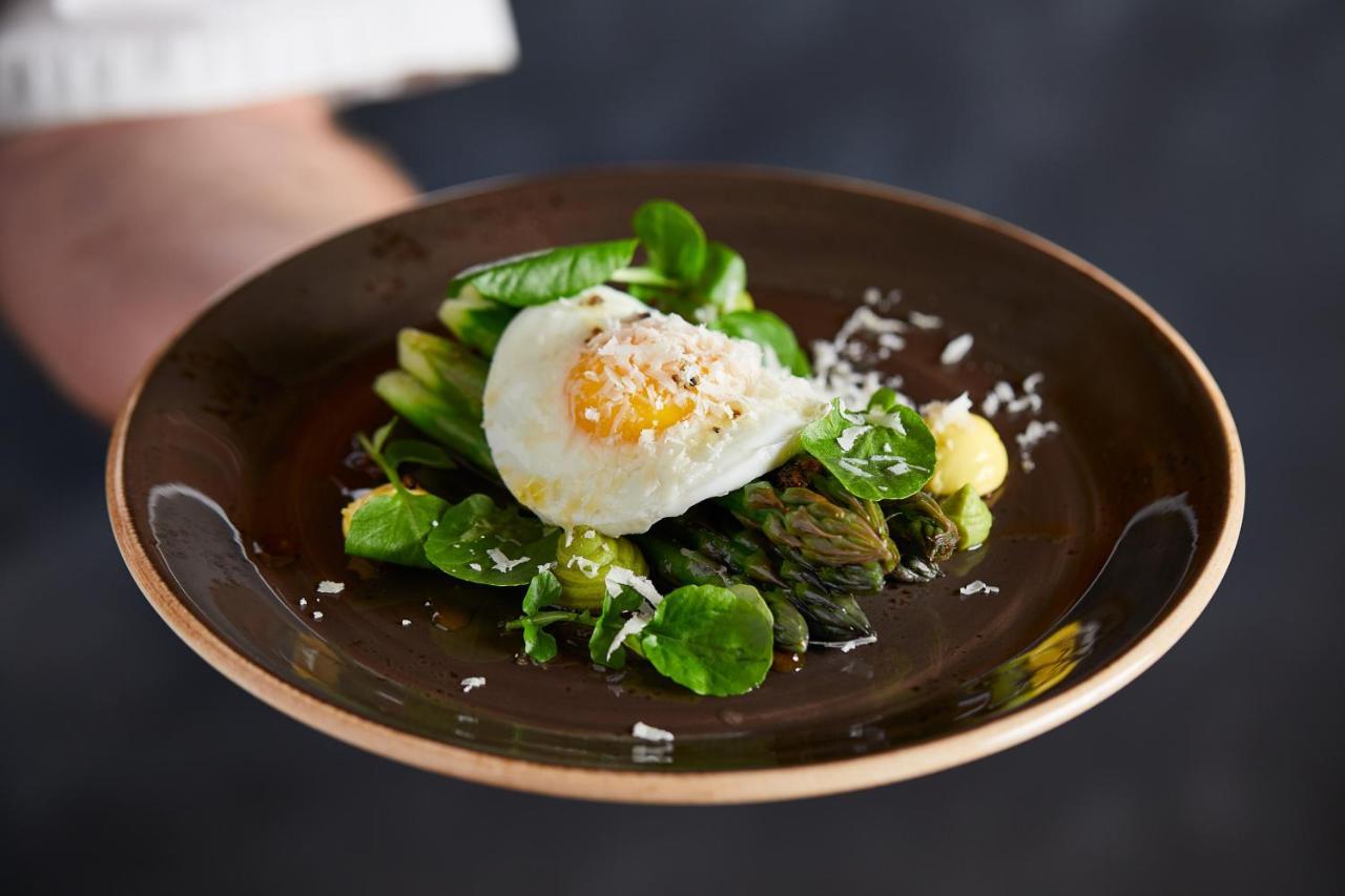 맥도날드 배스 스파 호텔 바스 외부 사진 The photo shows a plate of beautifully arranged food, featuring a poached egg on top of a mix of fresh greens. The greens include asparagus, lettuce, and possibly some herbs, garnished with a sprinkle of grated cheese or a similar topping. The dish i