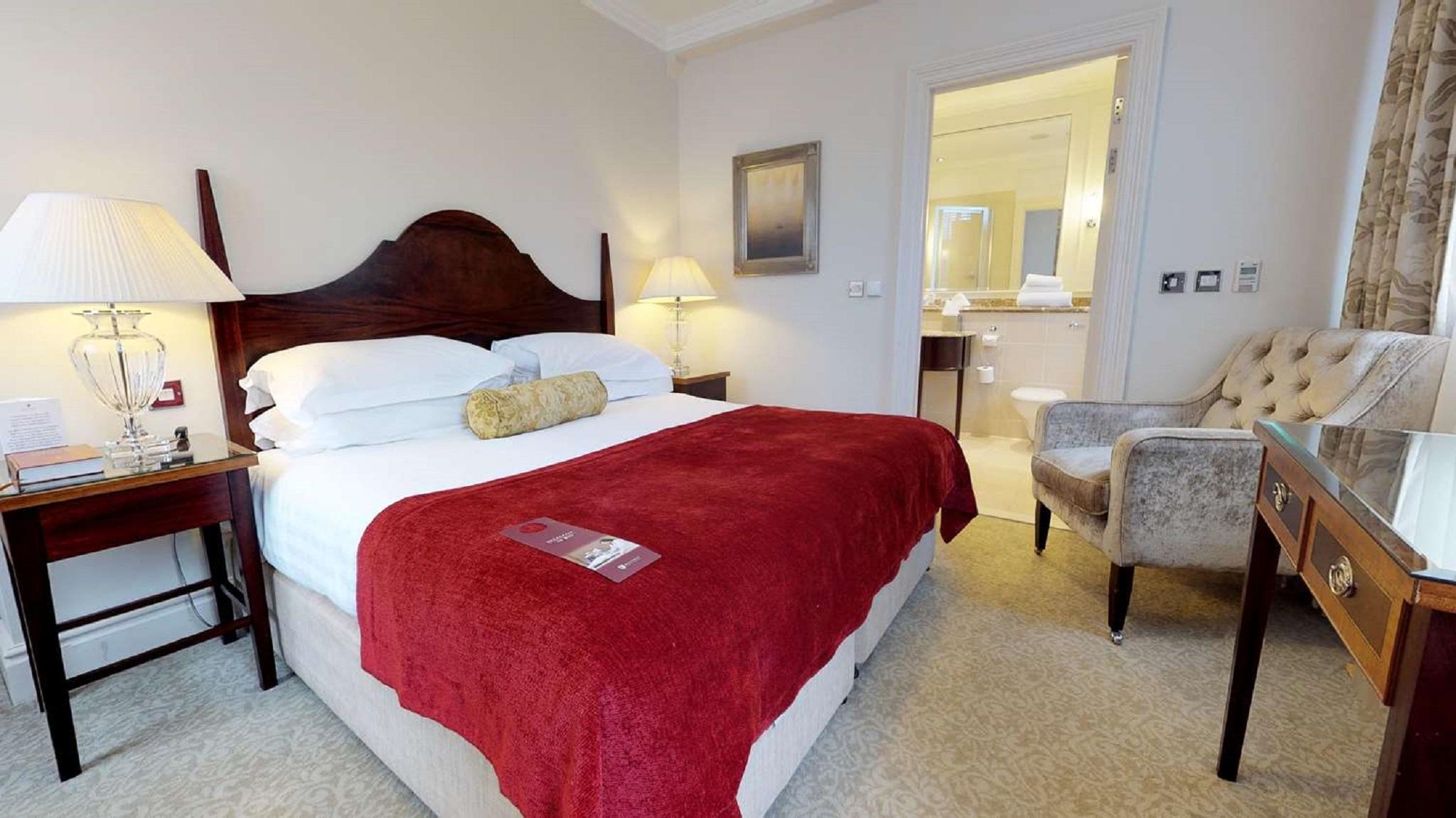 맥도날드 배스 스파 호텔 바스 외부 사진 The photo shows a well-furnished hotel room. In the center, there is a large bed with white linens and a red throw blanket. A decorative pillow is placed on the bed. On either side of the bed, there are bedside tables with lamps. To the right, there 