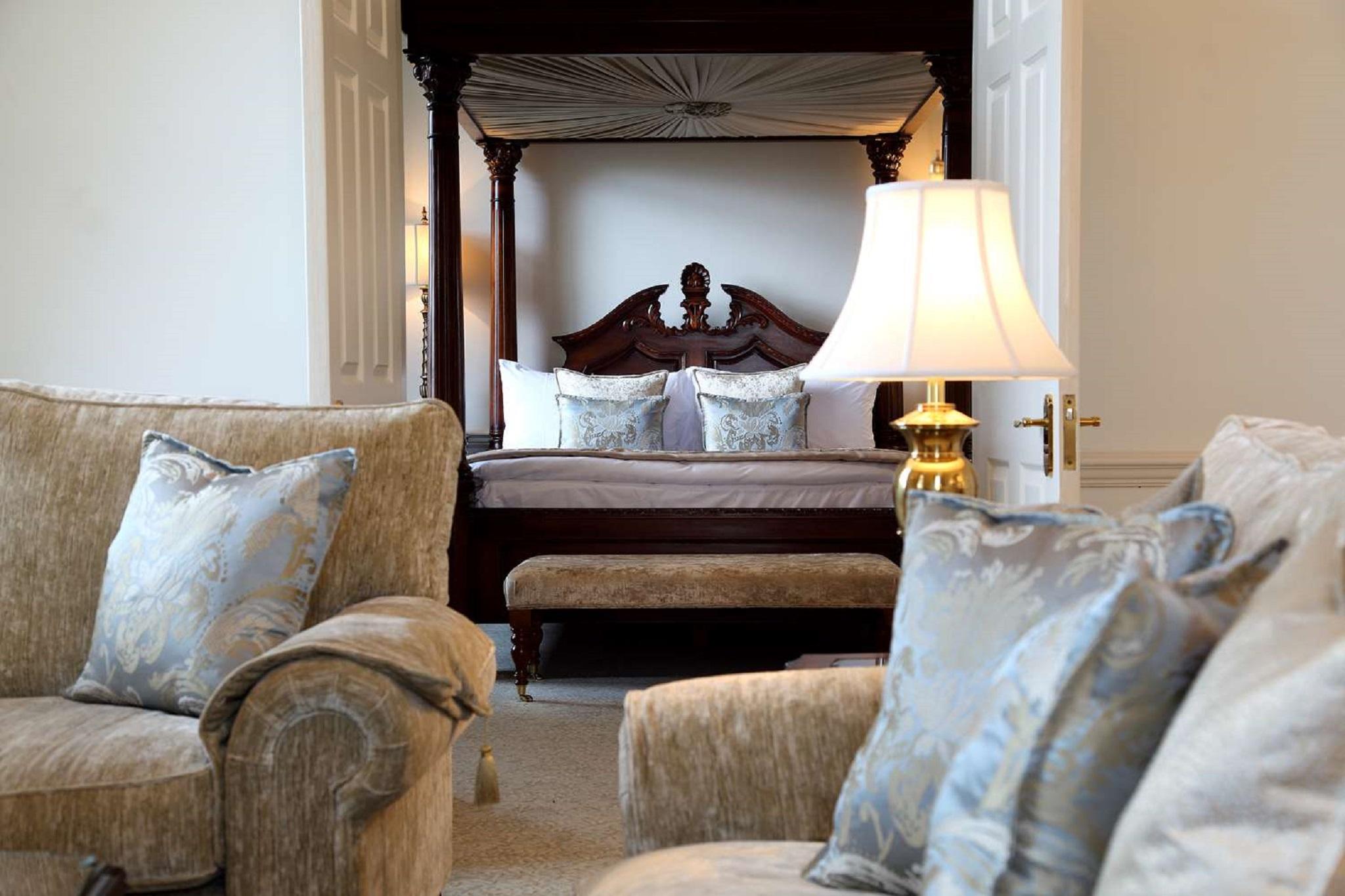맥도날드 배스 스파 호텔 바스 외부 사진 The photo shows a beautifully decorated room featuring a four-poster bed in the background. The bed has a wooden frame with a rich design, and it is adorned with plush bedding and pillows. In the foreground, there are comfortable sofas with decorativ