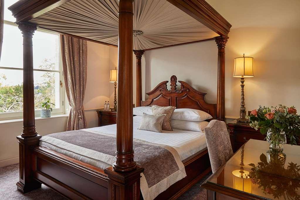 맥도날드 배스 스파 호텔 바스 객실 사진 The photo shows a beautifully designed bedroom featuring a four-poster bed made of dark wood. The bed has an elaborately carved headboard and is adorned with a light-colored bedding set. Above the bed, there is a canopy that adds an elegant touch. On
