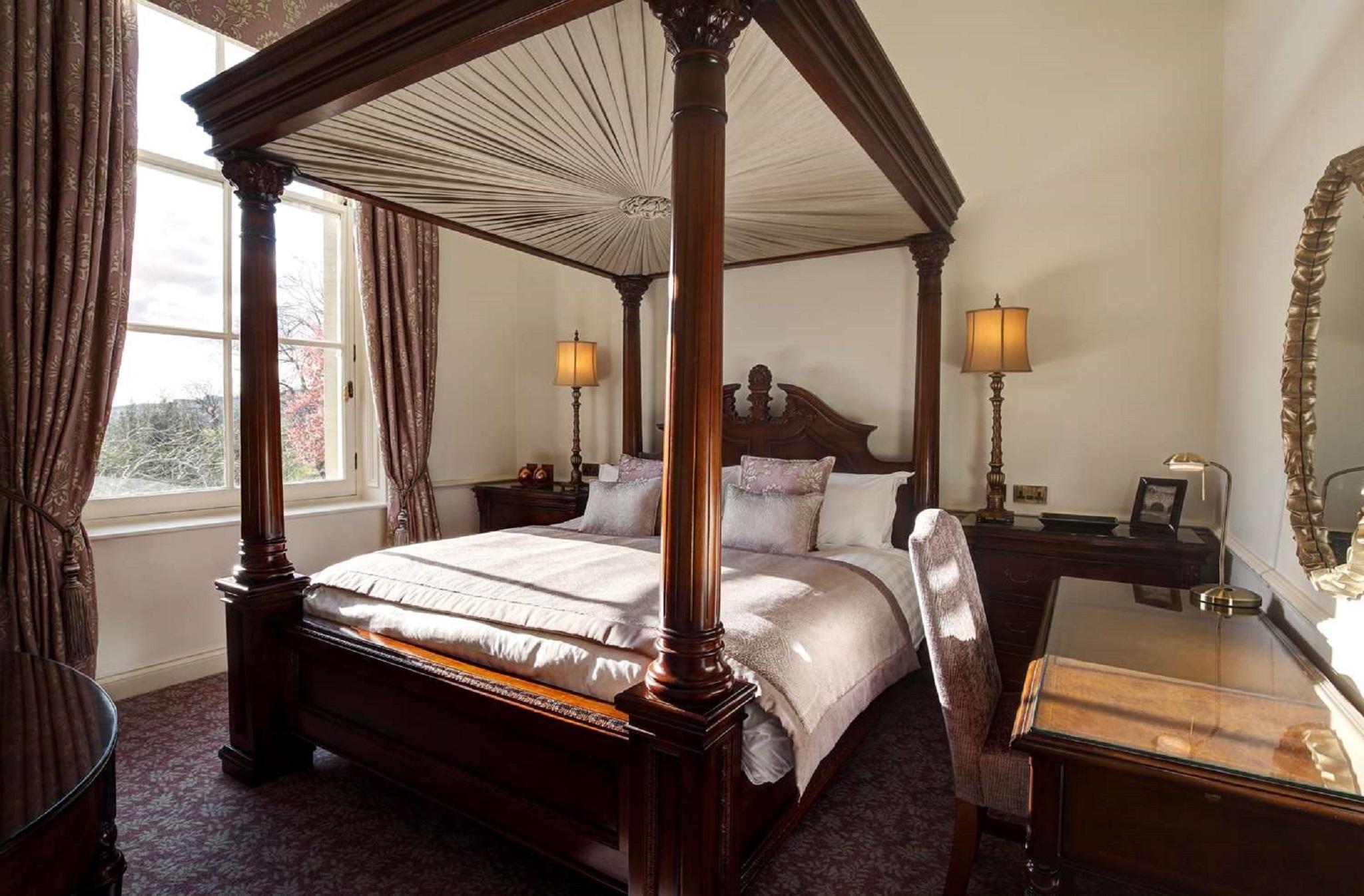 맥도날드 배스 스파 호텔 바스 외부 사진 The photo shows a well-decorated bedroom featuring a four-poster bed with an elegant wooden frame. The bed is dressed with light-colored linens and several decorative pillows. On either side of the bed, there are matching bedside lamps that provide s
