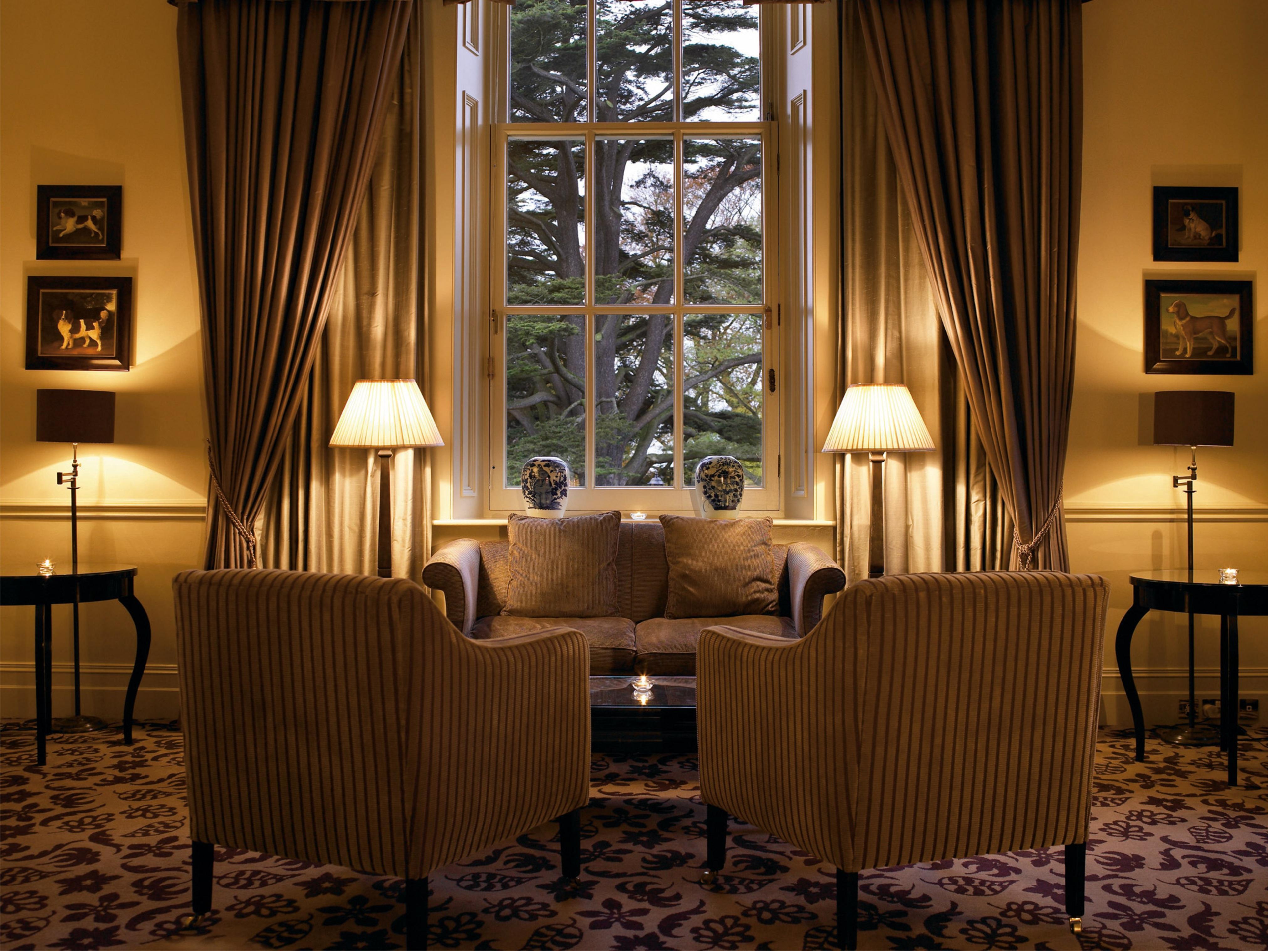 맥도날드 배스 스파 호텔 바스 외부 사진 The photo shows a cozy and elegant sitting area. There are two upholstered armchairs facing a small sofa, all arranged around a central coffee table. Soft lighting is provided by two lamps with white shades, one beside each chair. The window behind t
