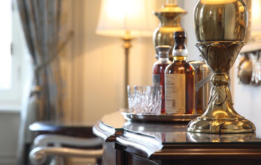 맥도날드 배스 스파 호텔 바스 외부 사진 The photo features an elegant interior scene that includes a polished wooden bar or table. On the surface, there are several bottles of liquor, likely whiskey, each with a distinctive label. A glass, possibly for drinking, is positioned near the bott