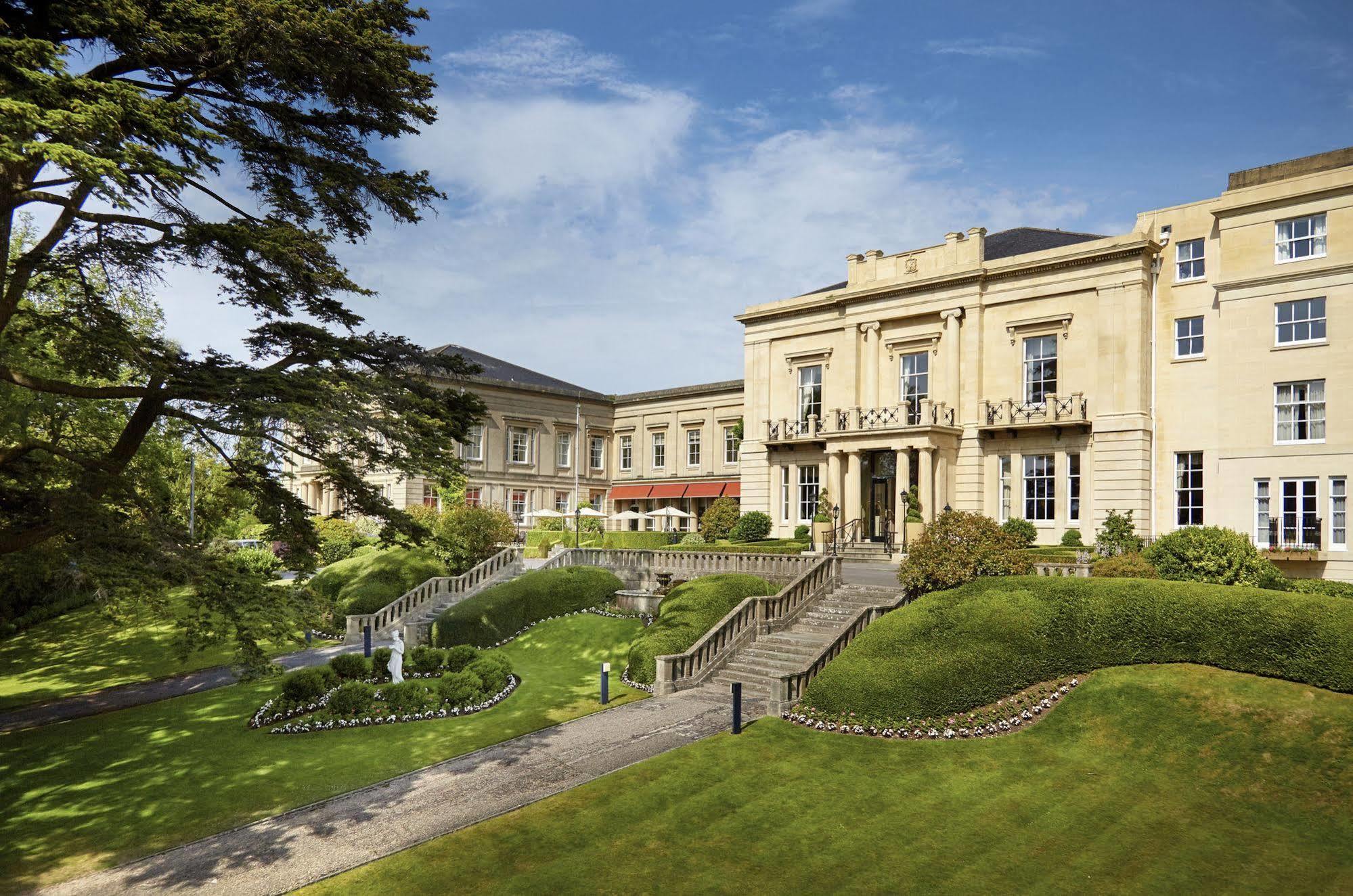 맥도날드 배스 스파 호텔 바스 외부 사진 The photo shows a grand building, likely a hotel or estate, surrounded by well-manicured gardens and lawns. The architecture appears elegant, with multiple stories and large windows. There are steps leading up to the entrance, and the setting include